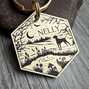 May include: Brass dog tag with a black silhouette of a dog, a crescent moon, and trees. The tag is engraved with the name "NELLY".