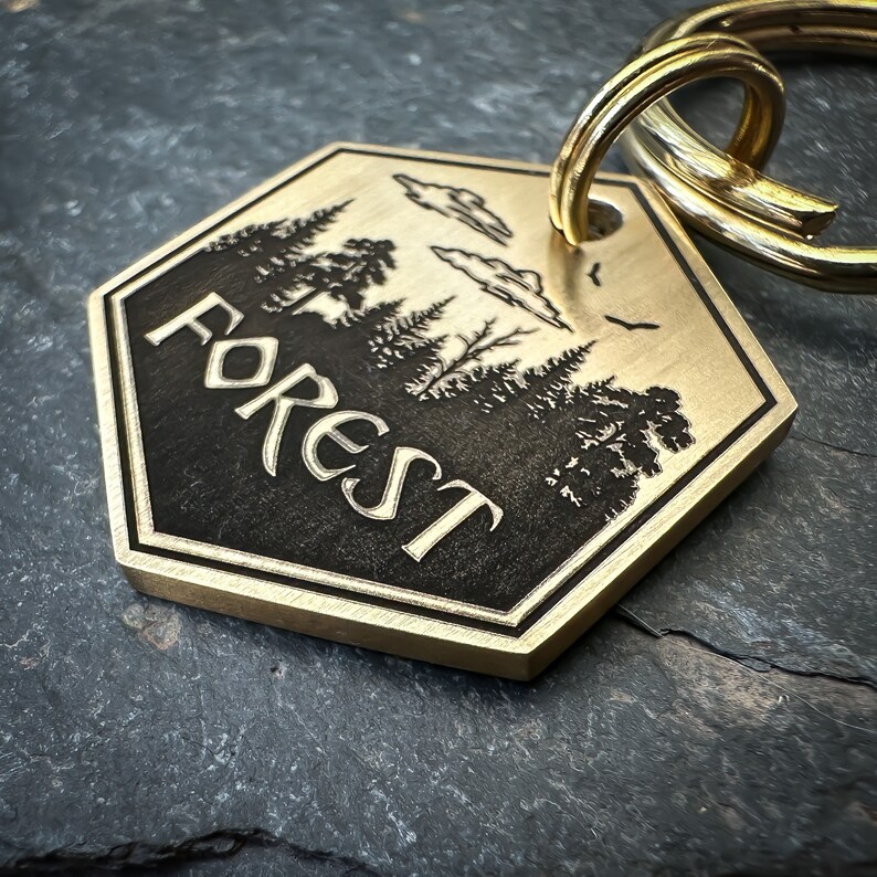 May include: A brass key chain with a hexagonal tag featuring a silhouette of a forest with the word "FOREST" engraved in a stylized font.