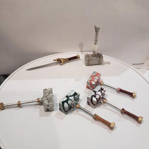 May include: Five miniature silver hammers with different colored accents, including red, green, and blue, and a silver sword with a gold handle.