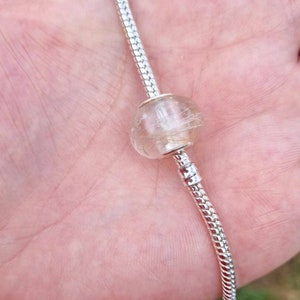 May include: A silver charm bracelet with a clear glass bead filled with white and gold hair.