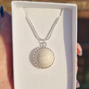 May include: A silver chain necklace with a white round pendant featuring a decorative silver border.