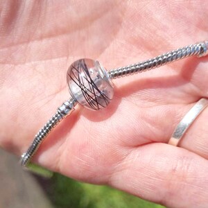 May include: A silver charm bracelet with a clear glass bead charm containing black strands of hair.