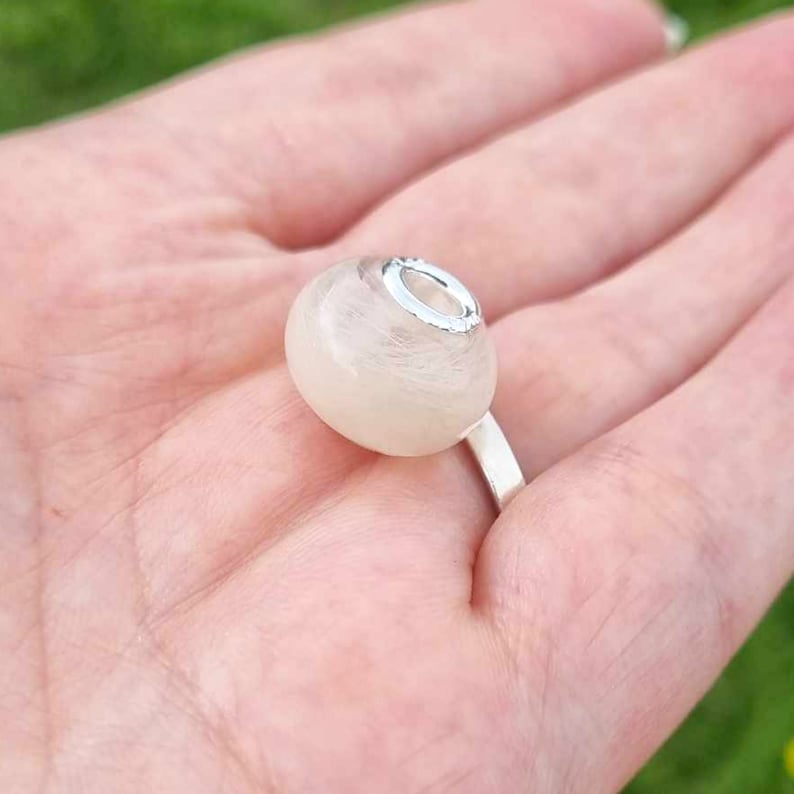 May include: A white glass bead with a silver metal ring. The bead has a swirl pattern.