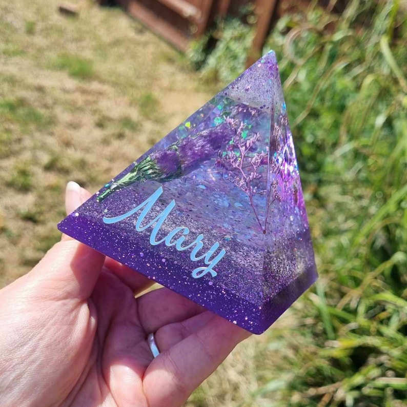 May include: A purple resin pyramid with embedded dried flowers and glitter. The name "Mary" is written in white on the front.