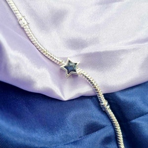 K&ouml;nnte beinhalten: Ein silbernes Armband mit einem sternf&ouml;rmigen Anh&auml;nger. Der Sternanh&auml;nger hat eine blaue und violette irisierende Oberfl&auml;che.