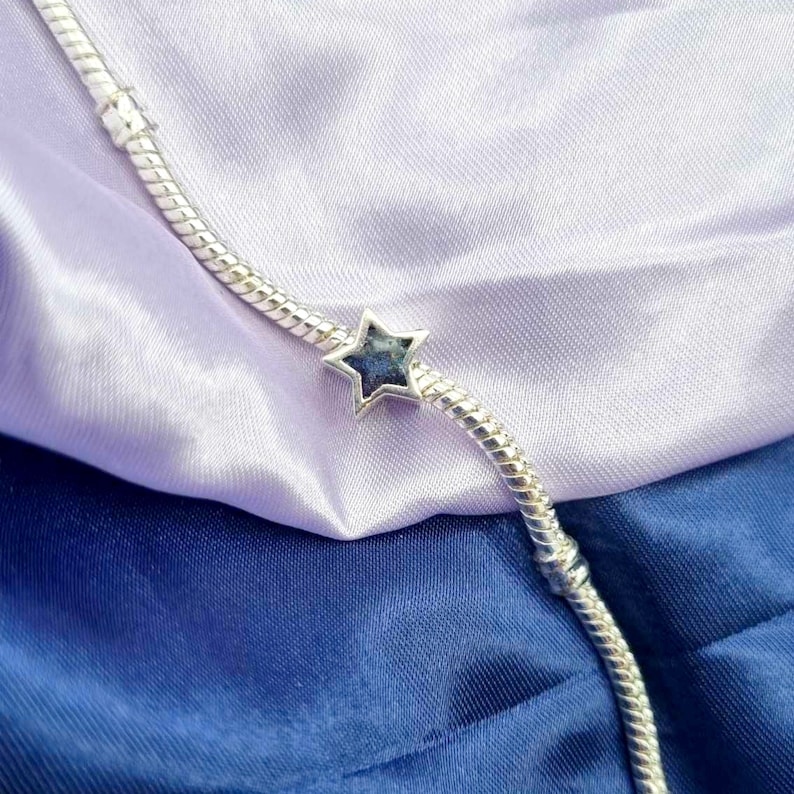 K&ouml;nnte beinhalten: Ein silbernes Armband mit einem sternf&ouml;rmigen Anh&auml;nger. Der Sternanh&auml;nger hat eine blaue und violette irisierende Oberfl&auml;che.