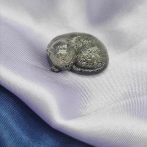May include: A small, grey, sleeping cat figurine made of stone.