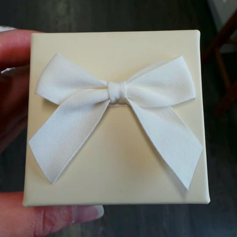 May include: A small, cream-coloured gift box with a white satin bow on top.