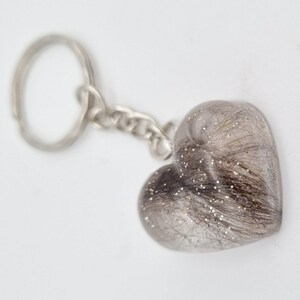 May include: A silver heart-shaped keychain with a clear resin insert containing a small amount of brown hair and silver glitter.