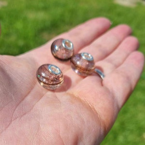 May include: Three glass beads with a silver metal core. The beads are filled with brown and white hair and have a shimmery finish.