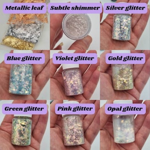 May include: Nine small glass jars filled with various glitter and metallic flakes. The jars are labeled with the following: Metallic leaf, Subtle shimmer, Silver glitter, Blue glitter, Violet glitter, Gold glitter, Green glitter, Pink glitter, and Opal glitter.