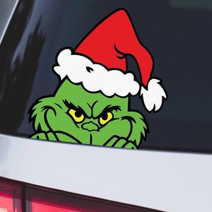 May include: A green Grinch character wearing a red and white Santa hat. The Grinch is peeking out from behind a surface, looking mischievous.