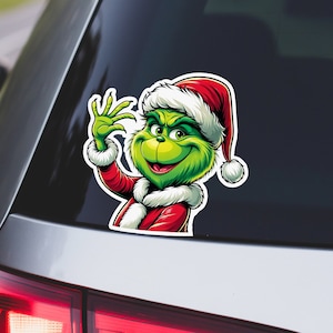 May include: A green Grinch character wearing a red Santa suit and a white Santa hat with a white pom-pom. The Grinch is smiling and waving with his right hand.