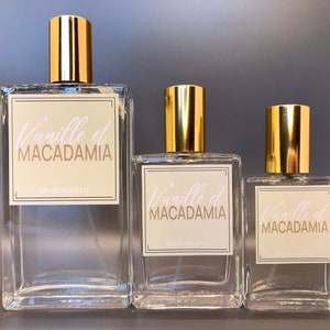 Three glass bottles of perfume, 100ml, 50ml and 30ml with gold caps and labels that say "Vanille et Macadamia" in white script. The bottles are different sizes.