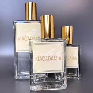 Three glass bottles of perfume, 50ml, 100ml and 30ml with gold caps and labels that say "Vanille et Macadamia". Nutty Vanilla perfume