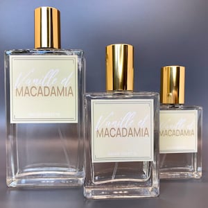 Three glass bottles of perfume with gold caps and labels that say "Vanille et Macadamia" in white script. The bottles are different sizes and are arranged from largest to smallest.