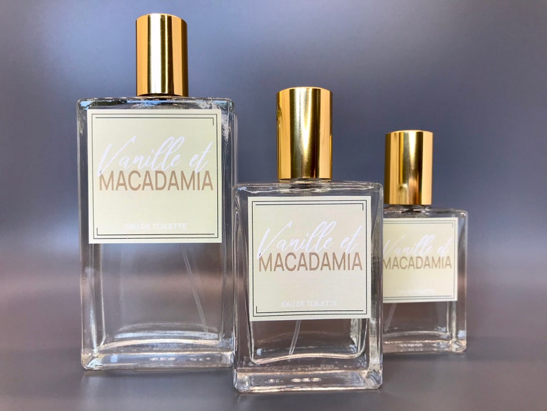 Three glass bottles of perfume with gold caps and labels that say "Vanille et Macadamia" in white script. The bottles are different sizes and are arranged from largest to smallest.