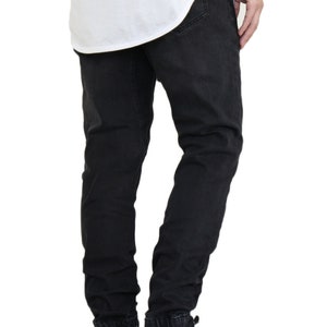 May include: Black jogger style jeans with a cuffed hem. The jeans are worn by a person wearing black and white sneakers.