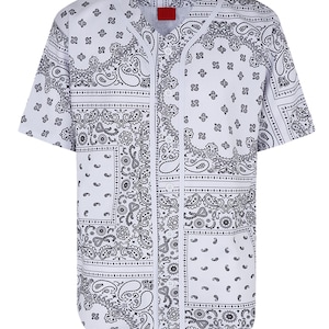 K&ouml;nnte beinhalten: Wei&szlig;es Baseball-Trikot mit schwarzem Paisley-Muster. Das kurz&auml;rmelige Hemd hat eine Knopfleiste vorne und ein rotes Etikett am Kragen. Das Design zeigt sich wiederholende Paisley-Motive.
