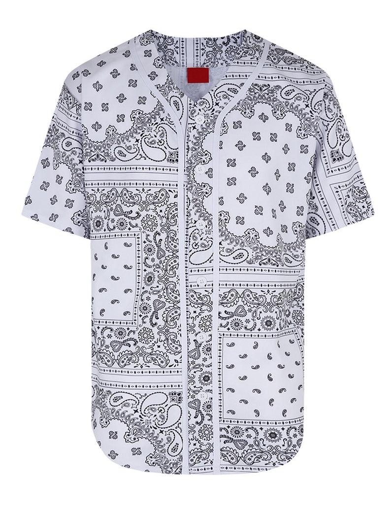 K&ouml;nnte beinhalten: Wei&szlig;es Baseball-Trikot mit schwarzem Paisley-Muster. Das kurz&auml;rmelige Hemd hat eine Knopfleiste vorne und ein rotes Etikett am Kragen. Das Design zeigt sich wiederholende Paisley-Motive.