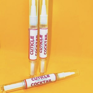 Könnte beinhalten: Drei durchsichtige Plastikflaschen mit weißen Kappen und rosa Etiketten. Die Etiketten zeigen "CUTICLE COCKTAIL cuticle oil".