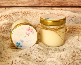 May include: Two small glass jars with gold lids and white labels. The labels have blue and pink footprints and the text "Girl or Boy". The jars are on a light brown fuzzy surface.