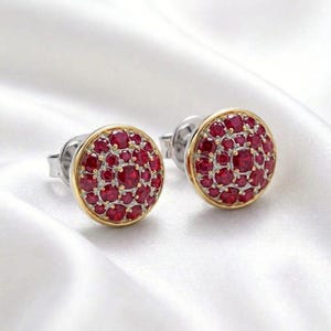 May include: A pair of round stud earrings featuring a cluster of small, vibrant red circular gemstones set in a silver-toned metal base with a thin gold-toned border. Each earring has a post back mechanism for secure attachment to the earlobe.