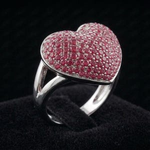 Peut inclure: Une bague argentée dotée d'une pièce centrale en forme de cœur. La surface du cœur est densément recouverte de nombreuses petites pierres rondes rouge foncé, serties étroitement pour créer un aspect texturé et rouge vif.