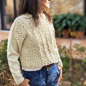 May include: A white crocheted sweater with a delicate openwork pattern. The sweater has long sleeves and a relaxed fit.