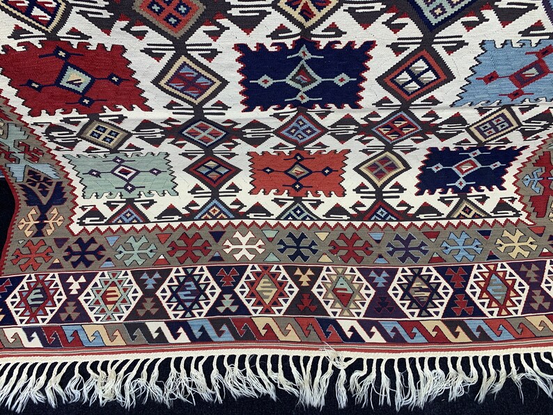 May include: A white rug with a geometric pattern in shades of red, blue, and green. The rug has a fringe border.