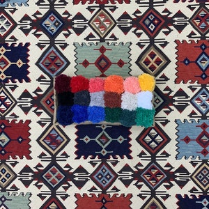May include: A colorful, rectangular pillow with a patchwork design. The pillow is made of different colored fabrics and has a fluffy texture. The pillow is sitting on a white and brown patterned rug.