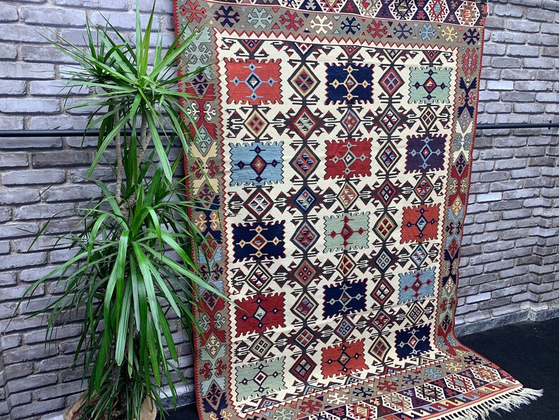 May include: A traditional rug with a geometric pattern in shades of red, blue, green, and white. The rug has a fringe border and is made of wool.
