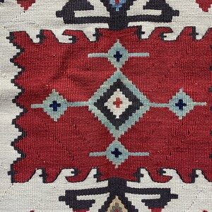 May include: Close-up of a red, white, and blue patterned rug with a geometric design. The rug has a traditional, hand-woven look.