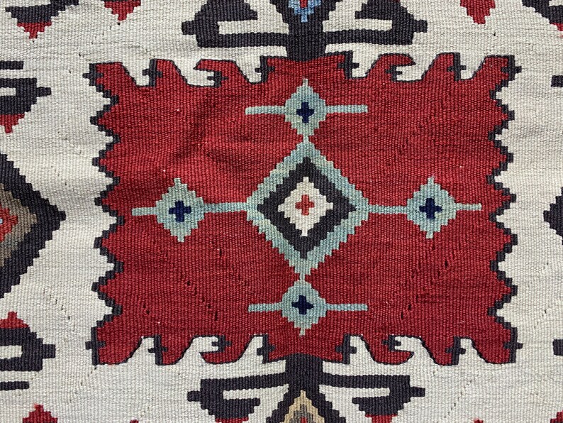 May include: Close-up of a red, white, and blue patterned rug with a geometric design. The rug has a traditional, hand-woven look.