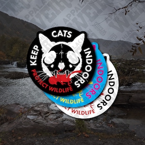 May include: Four round stickers with the text "Keep Cats Indoors" and "Protect Wildlife". The stickers are black, white, blue, and light blue. The black sticker has a skull and crossbones with a red lobster in its mouth.