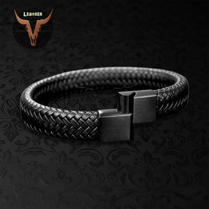May include: Black leather bracelet with a woven design and a square clasp. The bracelet features a braided texture and a matte finish. The image also includes a logo with the word "Leather" and a bull skull.