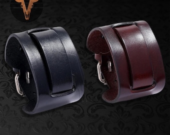 May include: Two wide leather cuff bracelets, one in deep black and one in dark burgundy, each featuring a smooth surface, a central strap detail, and a silver-toned metal buckle closure. The logo LEATHER with a bull skull icon is visible.
