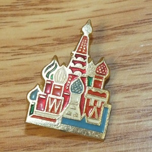 May include: A gold-colored pin with a red, white, and blue enamel design of the Kremlin in Moscow, Russia.