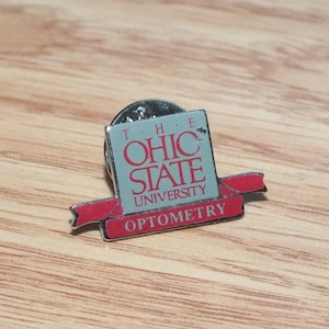 May include: A silver pin with a red ribbon. The pin features the text "The Ohio State University Optometry" in white lettering on a blue background.
