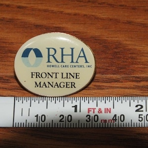 May include: A white and blue pin with the text "ORHA Howell Care Centers, Inc. Front Line Manager" on a gold background.