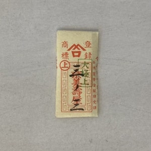 May include: A small, rectangular, cream-colored paper packet with red Chinese characters that read "商標" (Trademark), "金" (Gold), "銀" (Silver), "上" (Top), and "木板" (Wood Board).