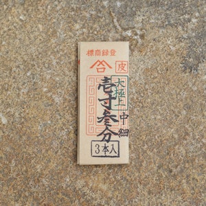 May include: A brown paper packet with black text that reads "標商録登 合 老寸会分 大極上中細 3本入".