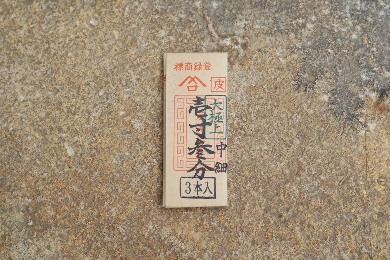 May include: A brown paper packet with black text that reads "標商録登 合 老寸会分 大極上中細 3本入".