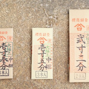May include: Three brown paper packages with Japanese text. The text includes the words "合" and "皮". The packages are labeled with the number of sticks inside: 3, 3, and 2.
