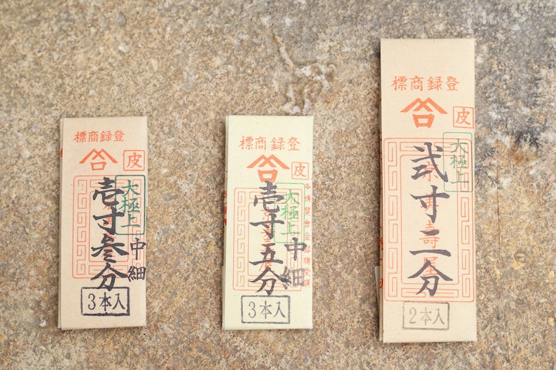 May include: Three brown paper packages with Japanese text. The text includes the words "合" and "皮". The packages are labeled with the number of sticks inside: 3, 3, and 2.
