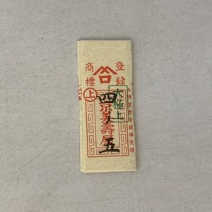 May include: A small, rectangular, cream-colored paper packet with red and green Chinese characters. The text reads "商標登録" which translates to "Trademark Registration".