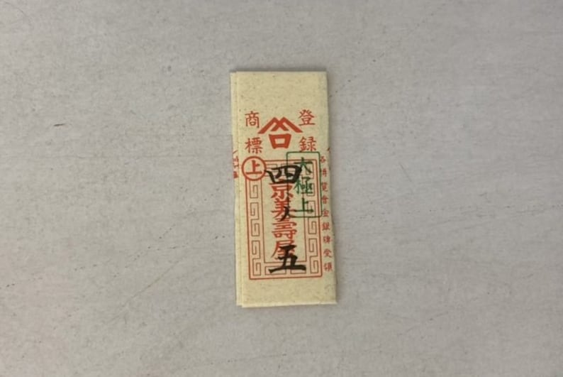 May include: A small, rectangular, cream-colored paper packet with red and green Chinese characters. The text reads "商標登録" which translates to "Trademark Registration".