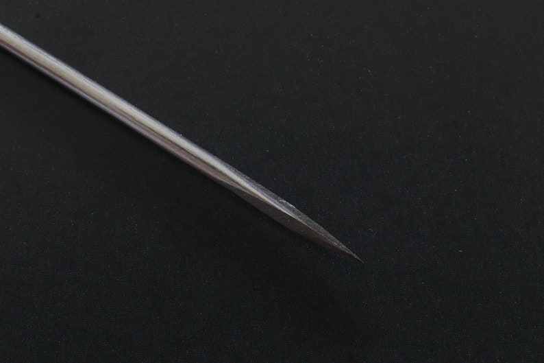 May include: A close-up of a silver, pointed, metal tool. The tool is thin and long, with a sharp point at the end.