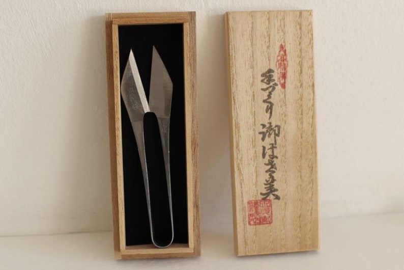 May include: A pair of silver scissors with a unique design, in a wooden box with Japanese writing on the lid. The writing reads "金寿堂"