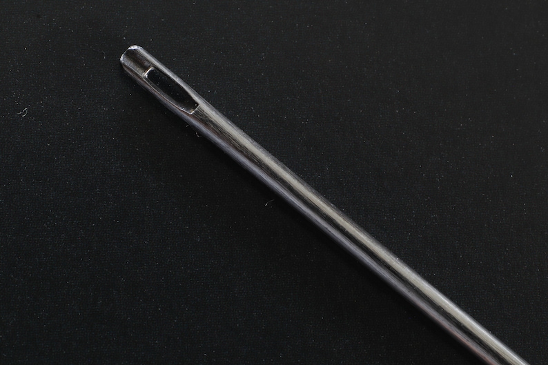 May include: A close-up of a silver sewing needle with a large eye.